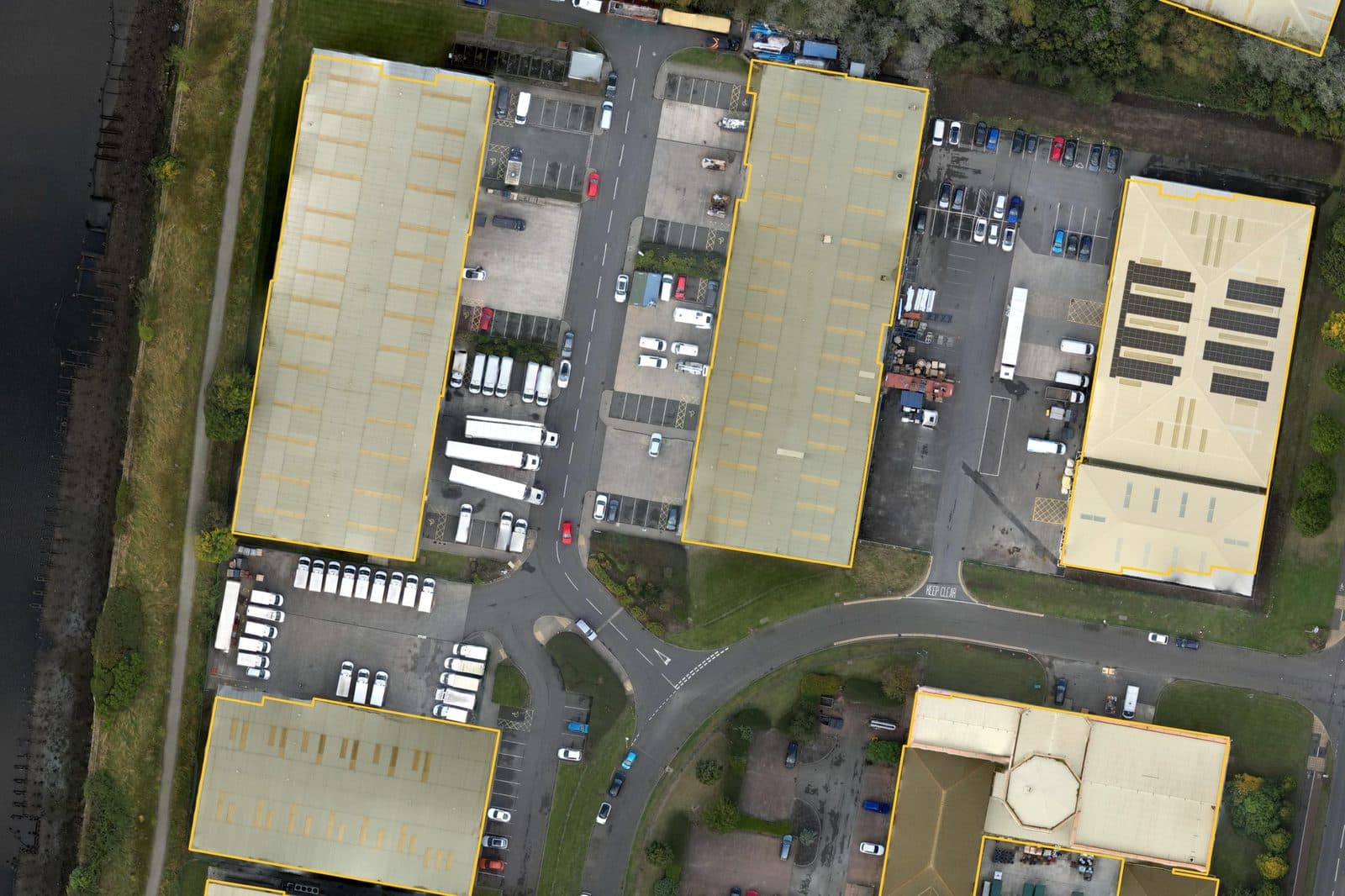 Aerial photo of warehouse sheds and yards on an industrial estate beside a river, roofs outlined in amber.